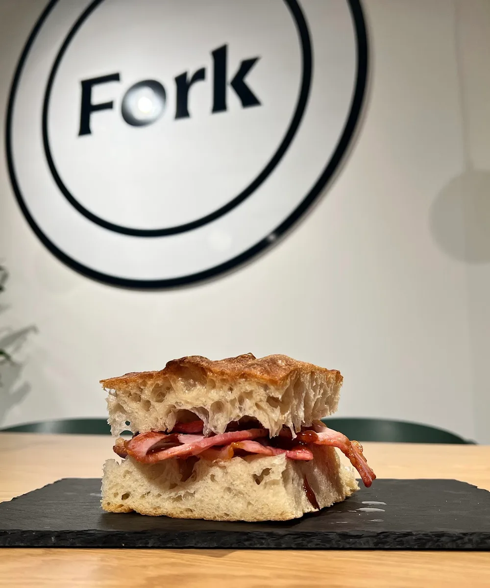 A focaccia sandwich served in front of the Fork wall sign